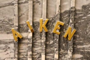 Aiken's name presented across "lyre strings" design on a the pedestal.